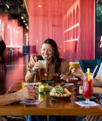 An image of four people sitting around a table and chatting with cocktails and appetizers on the table in front of them.