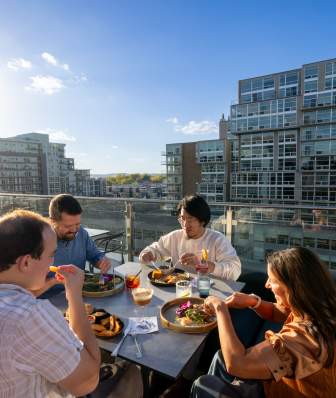 A group of friends enjoy their food while dining on a rooftop restaurant's outdoor patio.