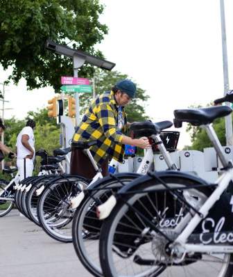 A woman in a plaid shirt removes an electric bike from a BCycle rental station.