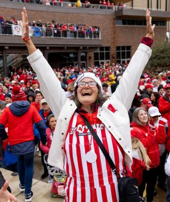 A white woman excitedly holds up her arms at a Badger tailgate