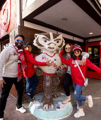 Family dressed in Badger gear poses next to Bucky Badger statue.