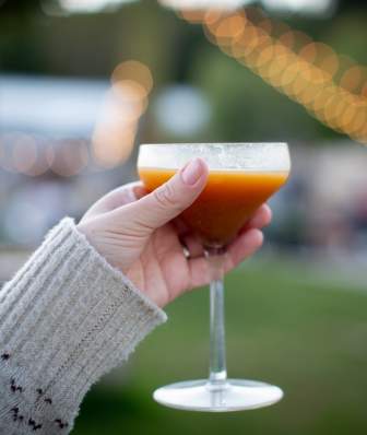 A close up of a person wearing a sweater holding up a fall cocktail