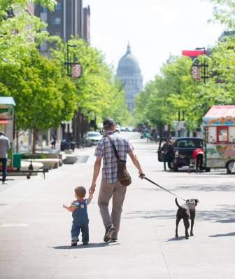 A man and child walking a dog down State Street in Madison