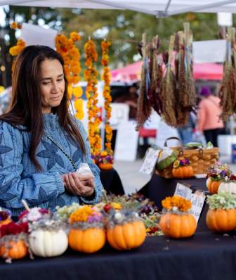 A woman looks at a table of flower arrangements made inside of small pumpkins at the Dane County Farmers' Market