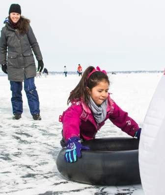 A girl slides on a tube into inflatable bowling pins on frozen Lake Mendota