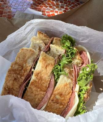 A photo of a large cold-cut sandwich in a takeout box