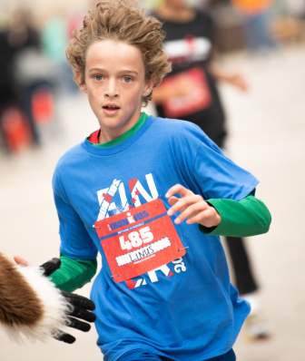 A young kid running in the IRONKIDS race. His hair is blowing in the wind