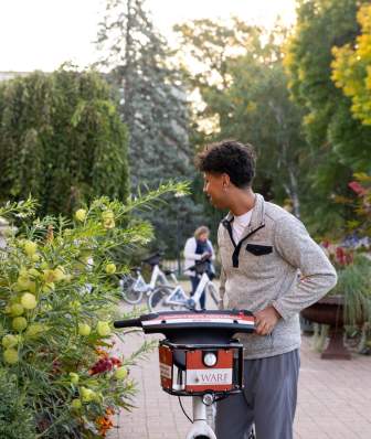 A young Black man wheels a bicycle through lush greenery at Allen Centennial Gardens