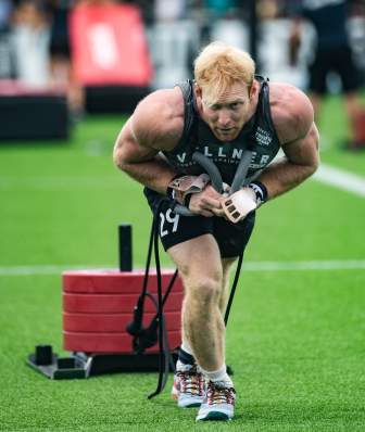 A man with red hair pulls a sled piled with red plates at the CrossFit Games