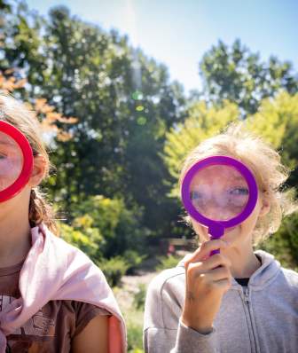 Two young white children hold magnifying glasses up to their faces at Olbrich Botanical Gardens