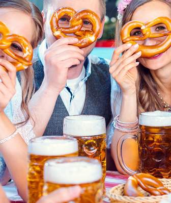 A group of friends hold pretzels up while enjoying a beer