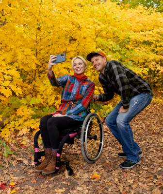A woman in a wheelchair and a man take a selfie while surrounded by yellow foliage at Picnic Point