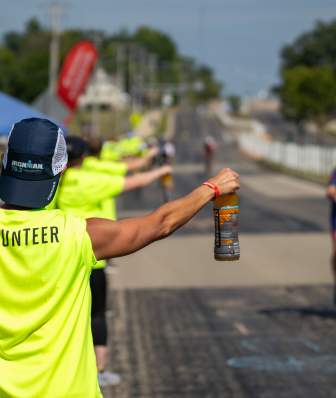 An image of a person volunteering at Ironman, handing a drink off to a biker