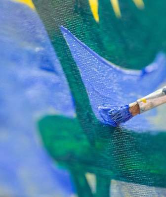 A white hand holds a paint brush and brushes blue on a canvas