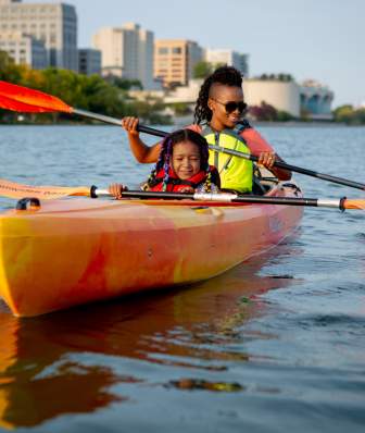 A Black woman and young Black girl kayak on Lake Mendota with the Madison skyline in the background