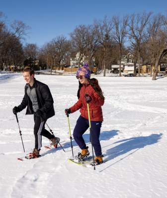 A couple snowshoeing over a frozen lake covered in snow on a sunny winter day.