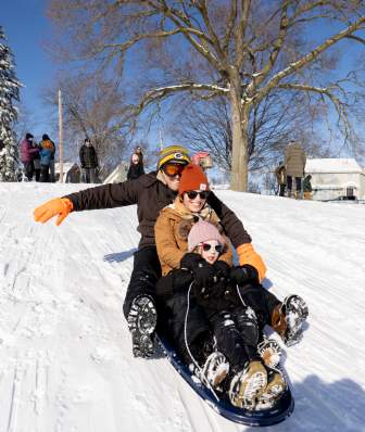 Two parents and their kid are bundled up in winter gear as they sled down a snow covered hill.