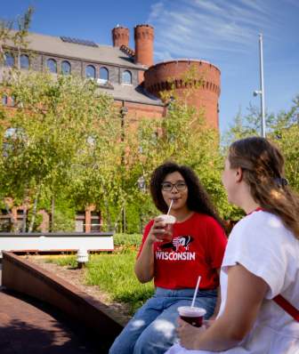 A Black woman and a white woman sit outside of the Red Gym on the UW Campus while they sip smoothies.