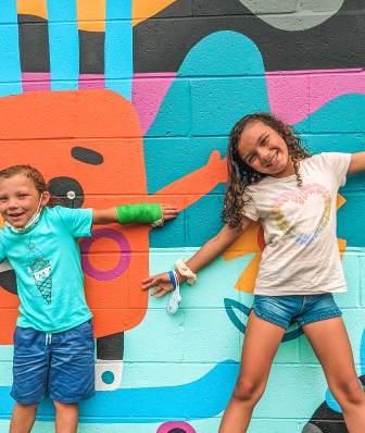 Two kids pose with a colorful mural