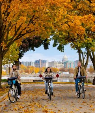 Three people riding bikes with the Capitol building in the background and a beautiful fall tree canopy