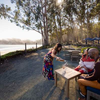 Couple wine tasting outside next to the beach with sun coming through eucalyptus trees