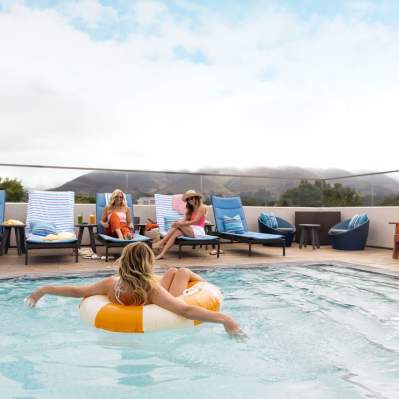 Person in an inner-tube in a pool with beach chairs and mountain in the background