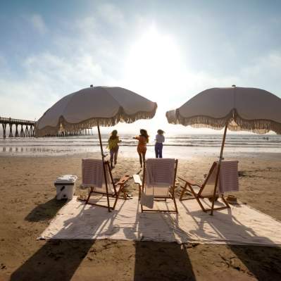 Beach chairs and umbrellas set up on the sand with women running towards the water in the background