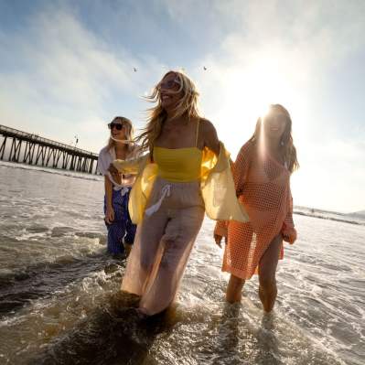 Three women walking through water near Pismo Pier with sun in background