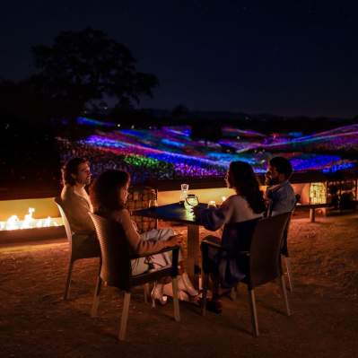 Group of four people at a table overlooking colorful lights in the distant hills
