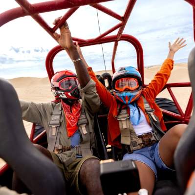 Two people with hands in the air and helmets on inside a caged dune buggy in Oceano, CA