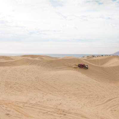 Car driving on large sand dunes with ocean in background