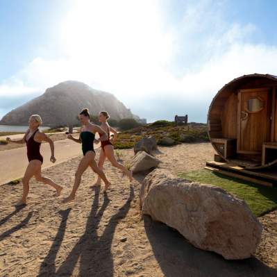 Three women running from the sauna to the bay with Morro Rock in the background