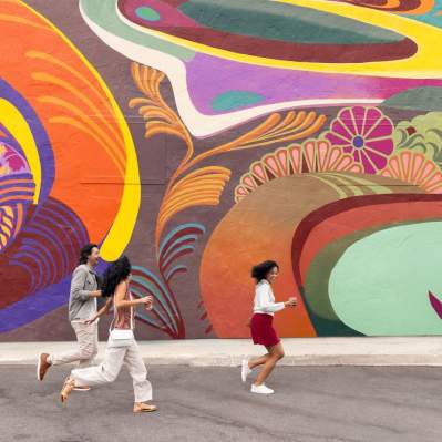 Three people running past a large colorful mural