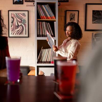 Women at bar looking at records in the background with other people in foreground with drinks