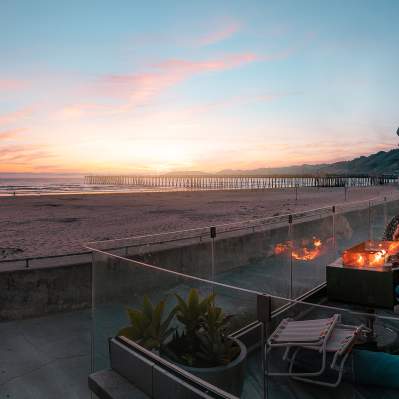 People watching sunset on a patio overlooking the beach with a firepit