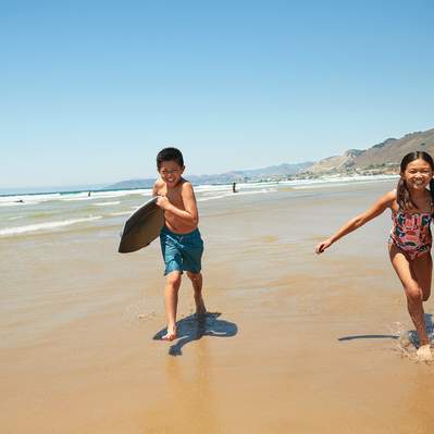 Two kids with boogie boards towards camera on the beach