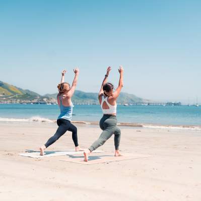 Two women doing yoga on the beach looking at the ocean