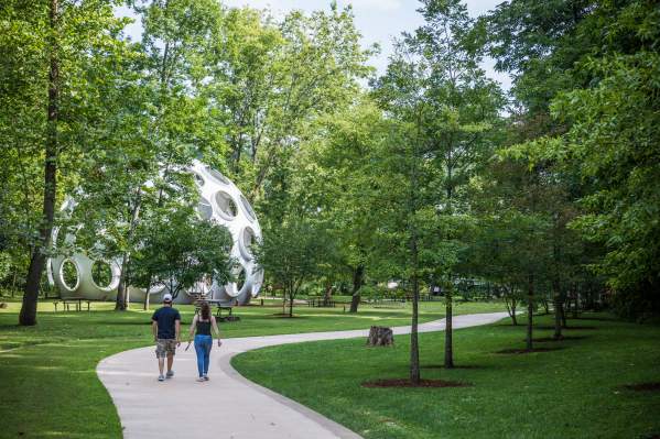A couple walking down a paved trail facing "Fly's Eye Dome"
