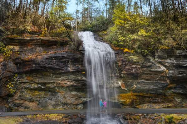 Man and Woman standing behind Bridal Veil Falls in Highlands, North Carolina.