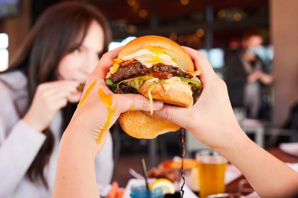 A messy burger is held up between two hands