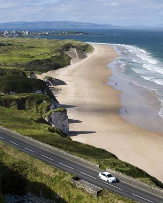 Aerial view of a car along the Causeway Coastal Route on a sunny day with the beach in the background