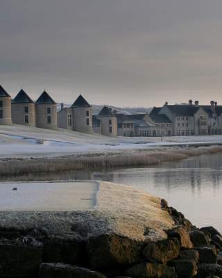 Snow-covered Lough Erne Resort reflected in a calm lake at winter sunrise, with two swans gliding across the water.