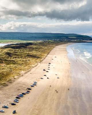 Aerial view of Portstewart beach with cars parked along the stretch of sand.