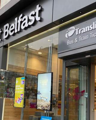 An exterior of the Belfast Welcome Centre with a tourist using a touch screen inside.
