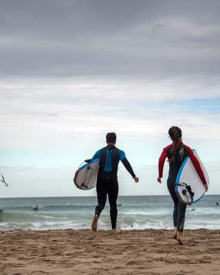 Four surfers running towards the sea to go Surfing at Whiterocks Beach, Portrush, County Antrim