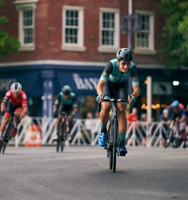 A professional cyclist rides in Centre Square past The Bayou restaurant during the 2022 Easton Twilight Criterium in Easton, Pa.