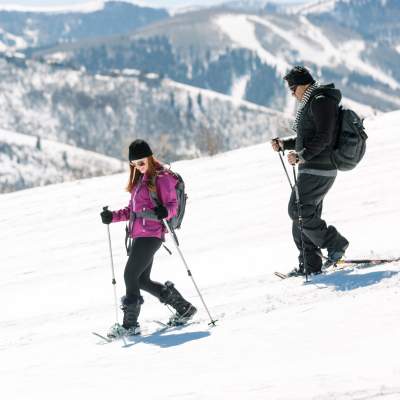 Couple snowshoeing down hill with ski resort in background