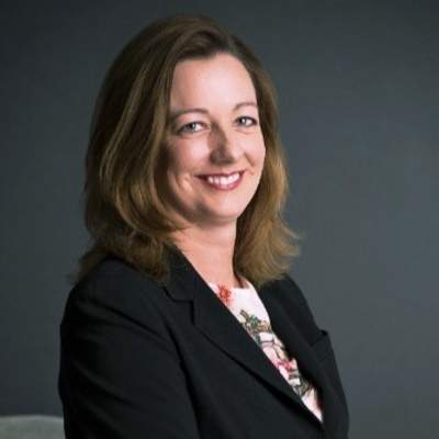 Morgen McLaughlin smiles in a dark blazer against a grey background.