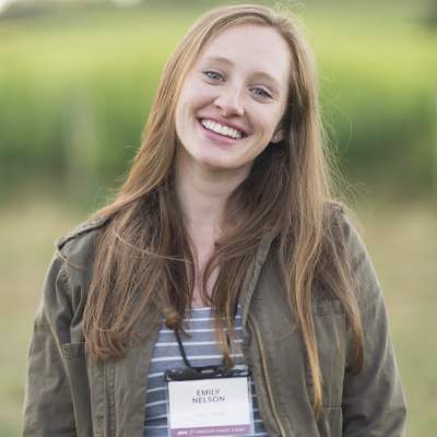 Emily Nelson smiles, sporting an Oregon Pinot Camp nametag, in front of a vineyard.