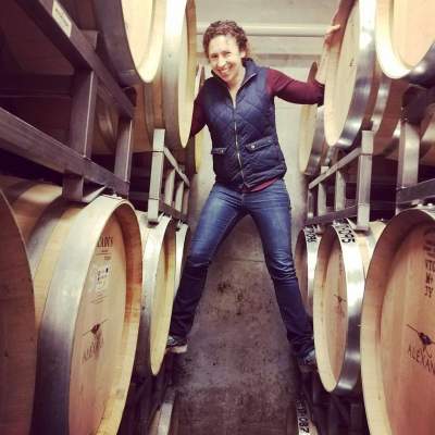 Julia Burke smiles while balancing on barrels in a wine cellar.